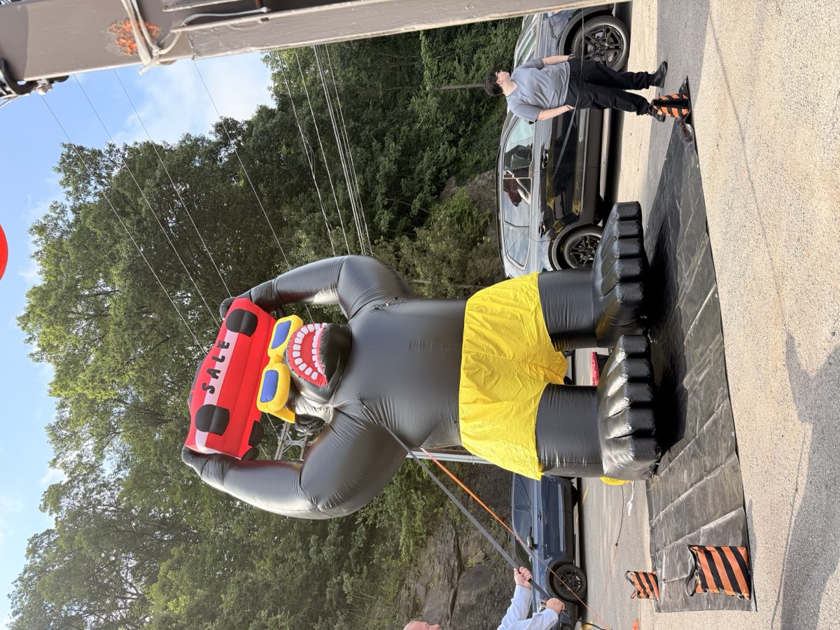 A large inflatable gorilla holding a car, set up on a dealership lot to draw attention to a sales event.