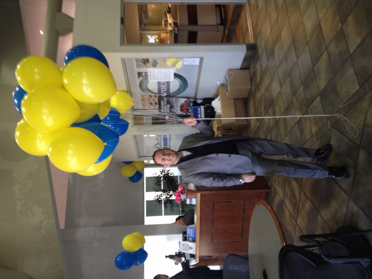 Steve Temes inside a dealership showroom decorated with blue and yellow event balloons.